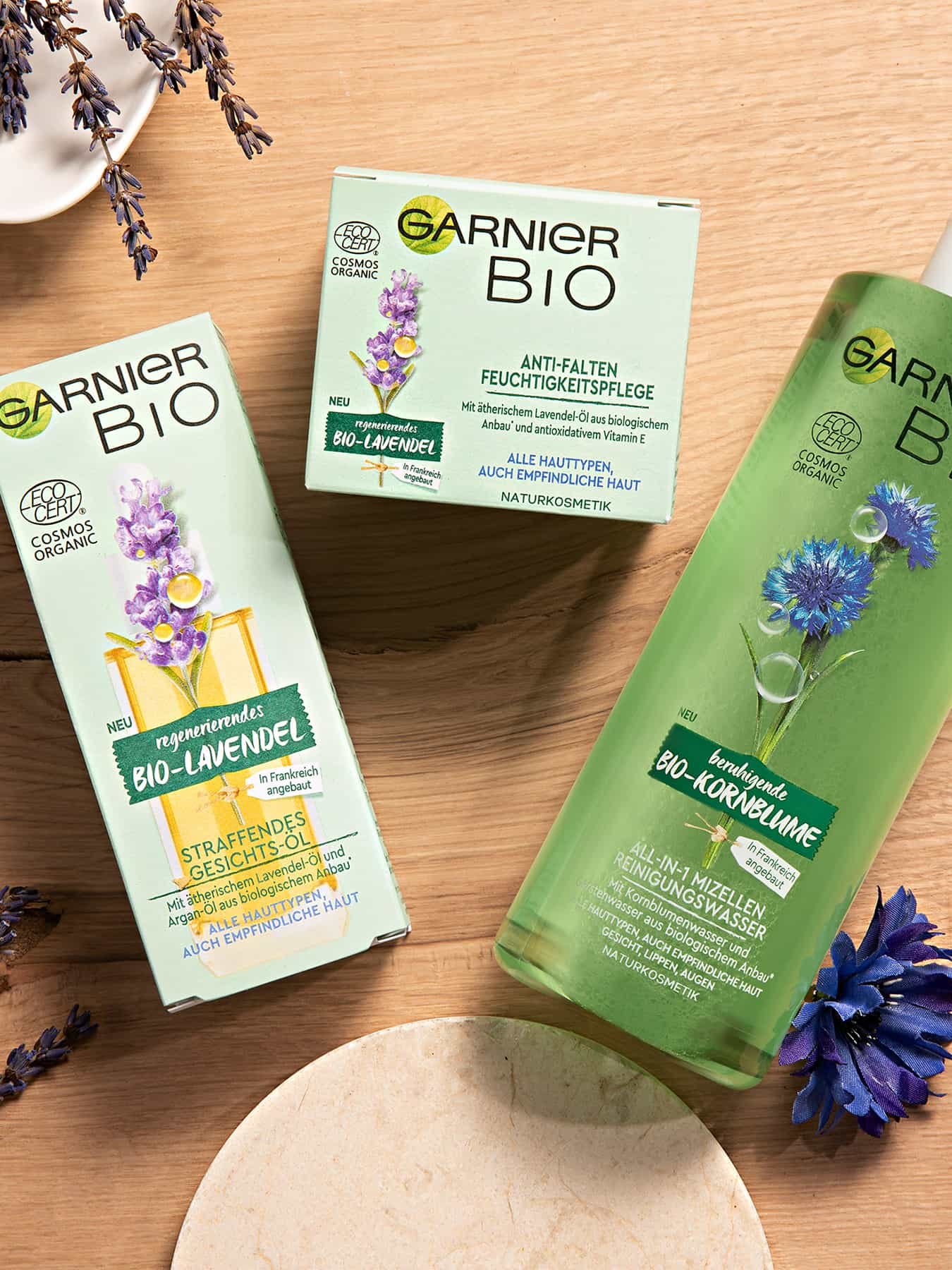 Garnier Produkte von oben auf einer Tischplatte, daneben Lavendel und eine Kornblumenblüte
